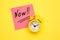 Sticker with handwriting the word NOW on alarm clock on yellow background with copy space using as stop procrastination