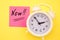 Sticker with handwriting the word NOW on alarm clock on yellow background with copy space using as stop procrastination