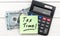Sticker with phrase `TAX TIME`, calculator and money on the wooden table. Top view