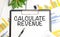 stickers, plant, pen and a white notebook with the text CALCULATE REVENUE