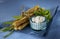 Sticks with feta cheese, tied with string, blue background, white dip, herbs
