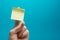 Sticky note, finger up of thumb, yellow reminder on blue background.