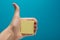 Sticky note, finger up of thumb, yellow reminder on blue background.