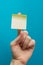 Sticky note, finger up of thumb, yellow reminder on blue background.