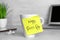 Sticky note with phrase Happy Boss`s Day attached to cup on grey table in office