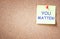 Sticky note pinned to cork board with the phrase you matter.