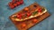 Still-life of appetizing bruschetta on wooden board. Close up of sandwich with melted cheese, bacon, cherry tomatoes