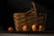 Still life of apples next to a vintage picnic basket against a black background