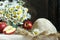 Still life with bouquet of daisies, straw hat and red apples on white tablecloth.