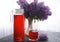 Still life with a bouquet of lilacs and compote of berries. A glass of compote, a jug, a bouquet, a book and glasses on a dark