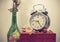 Still life with broken alarm clock, old glass vase with dead rose, perfume, vintage box, toned image.