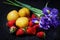 Still life on a dark table with irises, lots of strawberries and yellow plums with water drops