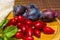 Still life - fresh large dogwood berries, purple plums and a sprig of basil on a wooden board