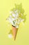 Still life with an ice cream cone, on a yellow background. In the bag there are many white flowers, so-called irises, which are in
