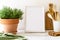 Still life in the kitchen with empty Mockup frame, thyme plant in a terra cotta pot, utensils on white wooden table.