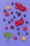 Still life of multi-colored berries on purple background. Red currants raspberries red and yellow, blueberries green mint