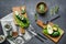 Still life, sliced cucumbers, avocados and kiwis lie on wooden boards against a gray background, glass jars with nuts stand rarely