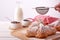 Still life with sugared Croissant, porcelain bowls with fruit jam and glass of milk and female hand with sugar, on white wooden