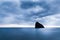 Still sea waters, harsh rocks and cross on rock peak in evening on summer day with gloomy sky at background