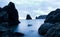 Still sea waters, harsh rocks and cross on rock peak in evening on summer day with gloomy sky at background