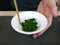 Stir fresh green tea leaves in white cup with chopsticks