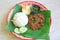 Stir-fried minced pork with basil leaves served with rice and fried egg on banana leaf on zinc tray over wooden table background