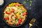 Stir fry egg noodles with shrimps, paprika, green pea, chives and sesame seeds bowl. Asian cuisine dish. Black kitchen table