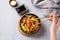 Stir-fry with soba noodles, meat and vegetables in black plate on a light background with hand hold chopsticks