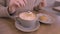 Stirring latte coffee with a spoon and a cookie lying on a plate. Action. Close up of woman hand stirring foam of her