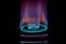 Stock photo of gas burner with blue and purple flame on kitchen stove in dark black background, focus on object