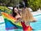 Stock photo of two girls of different ethnicities in the water of a swimming pool with a raised lgtb flag