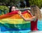 Stock photo of two girls of different ethnicities in the water of a swimming pool with a raised lgtb flag