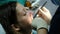 Stomatologist changes the cotton swab in the mouth of the woman, the assistant shines with a dental polymerization