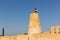 Stone arabic watchtower with waving United Arab Emirates National Flag in Al Jazirah Al Hamra, UAE