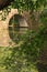 Stone Archway Bridge Reflected in River, Seen Through Foliage