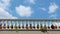 Stone balustrade of a balcony with flowers between the columns. Blue sky with fluffy clouds on background.