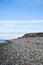 Stone beach by the sea. Flagpole with Danish flag on a hill. Danish coast