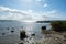 Stone breakwater on a coast in the sea, with a sailing ship on the horizon and a bright sun