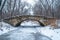 A stone bridge spans over a frozen river, with surrounding trees creating a picturesque winter scene, An old stone bridge over a