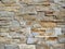 Stone cladding wall made of striped stacked slabs and blocks of brown and gray natural rocks.