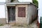 Stone and concrete small house with dilapidated cracked wooden doors and closed window blinds with new white metal gutter