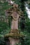 Stone cross tombstone decorated with two cherubs and covered with ivy