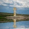 Stone cross on the waterfront. Reflections. Concept- faith, hope