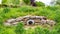 Stone drain and a round metal grid in a park surrounded by green vegetation