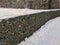 Stone fence made of metal mesh is covered with snow. Metal mesh with large stones. The stones are tightly stacked with each other