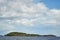 stone island overgrown with trees in the middle of the water. blue sky with clouds. northern landscape