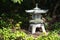 Stone lantern in shadow between evergreen ground cover plants pa