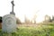 stone monument/tombstone with bitcoin symbol standing in green grass on cementery in front of stone cross - wide angle view