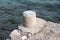 Stone mooring bollard on edge of concrete pier next to sea