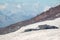 Stone outlier on red slope of Elbrus volcano with white glacier, clouds and Caucasus mountains in day time.